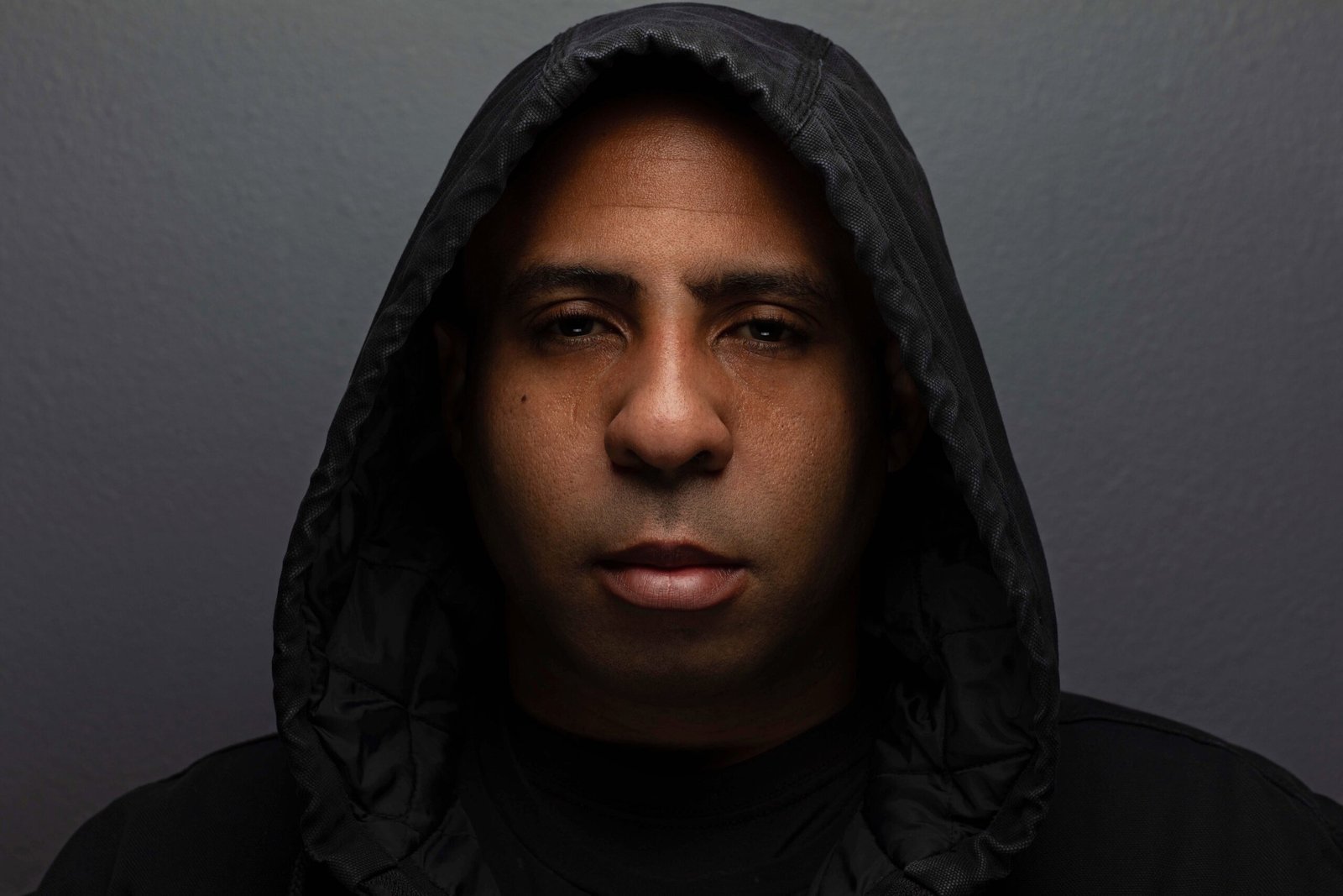 Jamin Camp wearing a dark hood, photographed against a grey background.